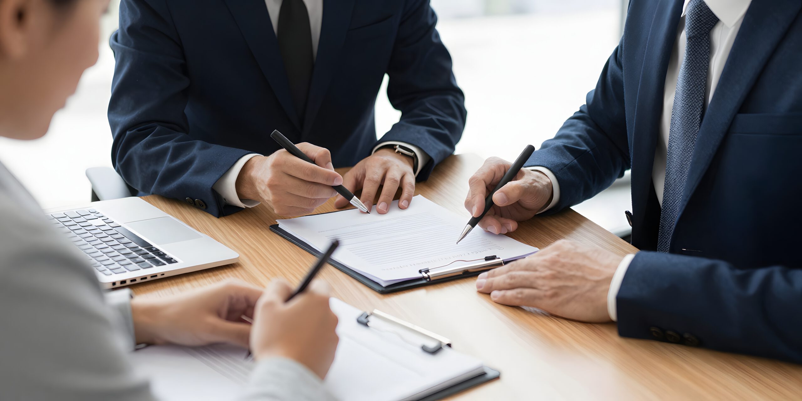 People in suites around a table, discussing a document, representing the business law services of Elysium Legal in Montréal, Ottawa, and Toronto. Des personnes en costume autour d’une table, discutant d’un document, illustrant les services en droit des affaires d’Elysium Légal à Montréal, Ottawa et Toronto.